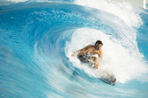 Action shot of man in swimsuit skillfully surfing inside the curl of a manmade wave at Palm Springs Surf Club.