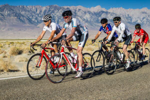Group of cyclists riding on a paved road with mountains in background.